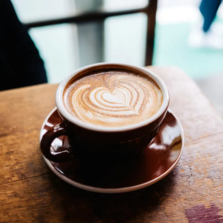 A flat white with heart latte art on a wooden table