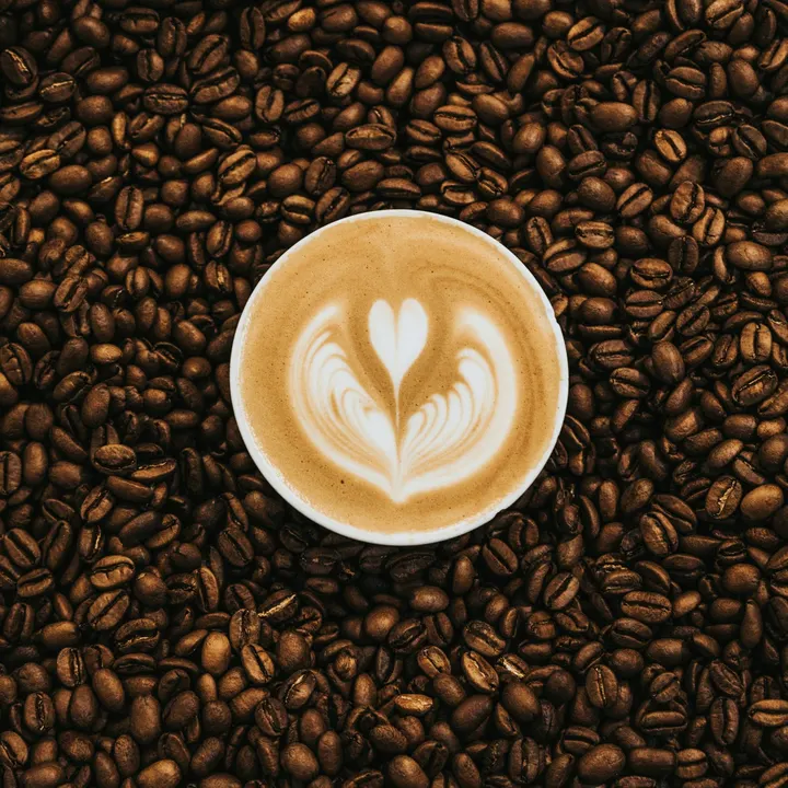 A latte with tulip art, surrounded by coffee beans