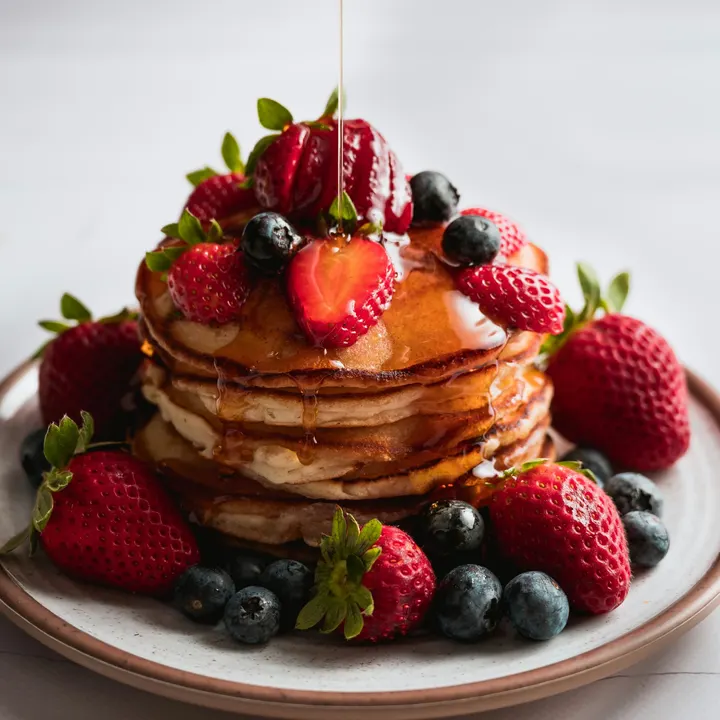 A stack of pancakes with strawberries, blueberries and maple syrup