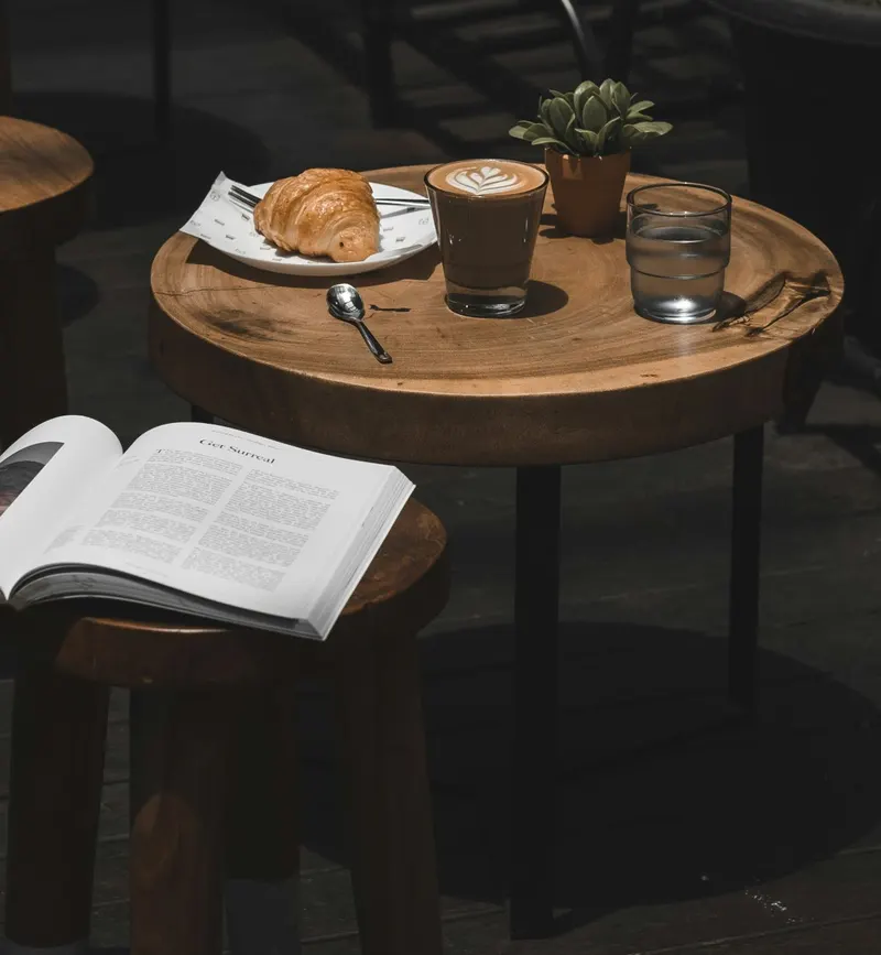 A flat white and a croissant on a small wooden table